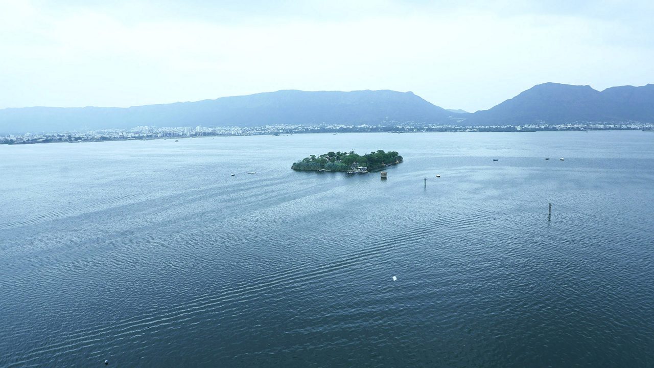The white marble Baradari pavilions of Shah Jahan standing along the stone embankment of Ana Sagar Lake in Ajmer, with the Aravalli hills behind the water